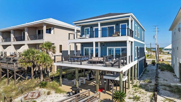 A beachfront property with a two-story building, a covered deck, and outdoor seating. - The Drift Away (Navarre Beach)
