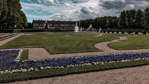A formal garden with a fountain, neatly trimmed hedges, and a large building in the background. - Apartment Balsberg southwest with 2 bedrooms and large balcony with mountain view (Unterwössen)