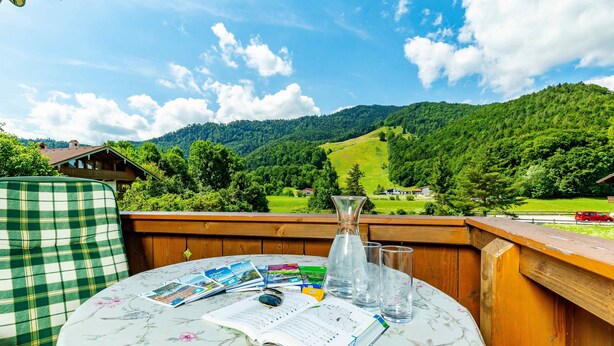 A wooden deck with a table set for reading, overlooking a mountainous landscape. - Apartment Balsberg southwest with 2 bedrooms and large balcony with mountain view (Unterwössen)