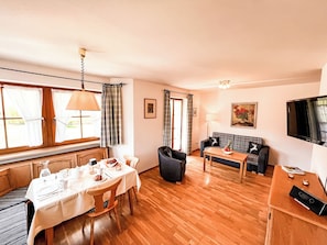 A living room with a sofa, a dining table set for four, a TV, and a painting on the wall.