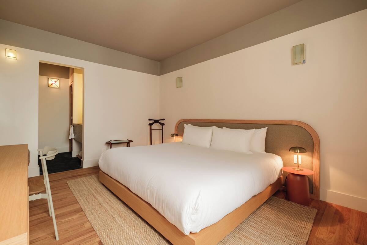 A neatly arranged bedroom with a large bed, bedside tables, a chair, and a small desk.