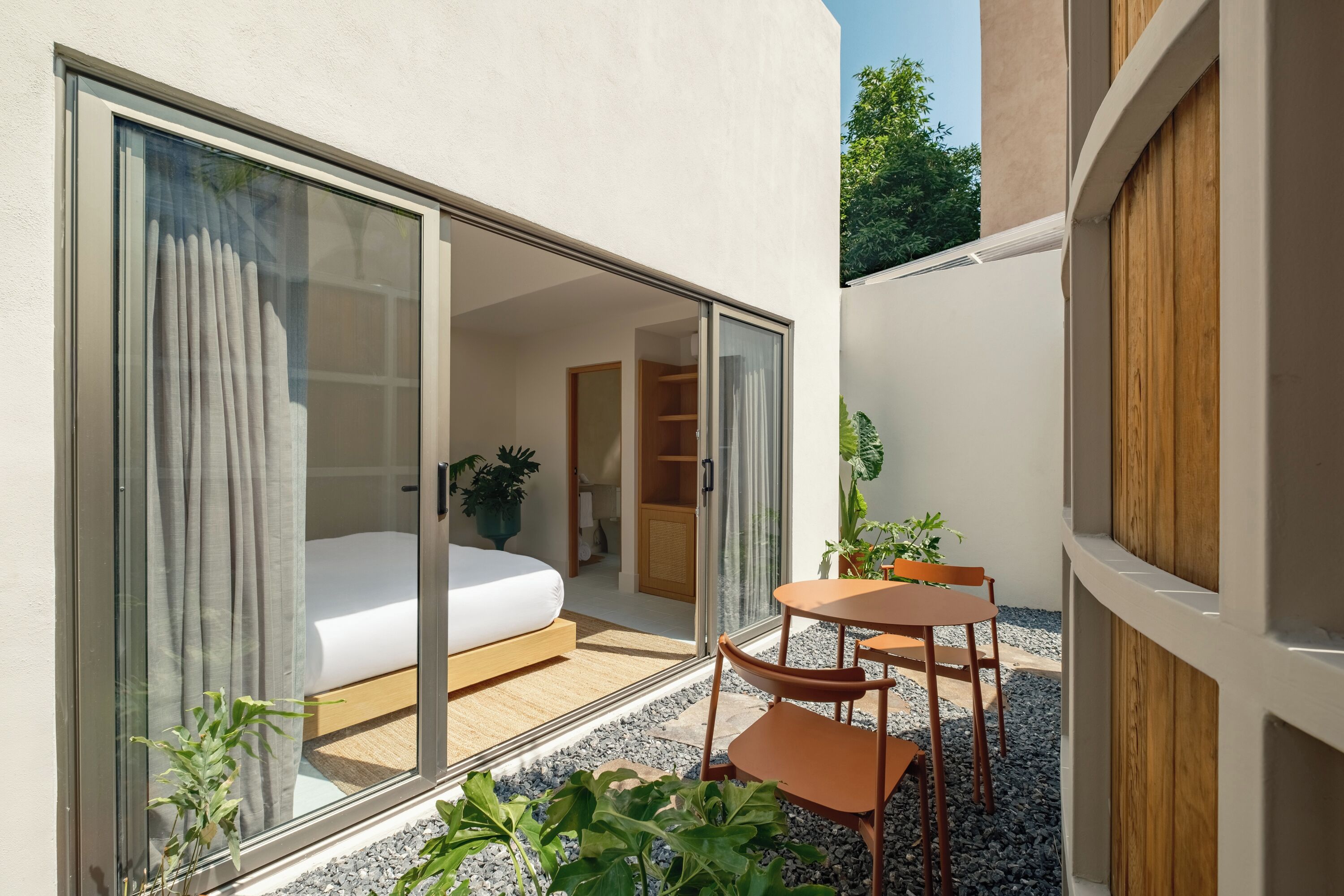 A modern hotel room with a sliding glass door leading to a balcony, a bed, a small table, and chairs.
