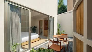 A modern hotel room with a sliding glass door leading to a balcony, a bed, a small table, and chairs.