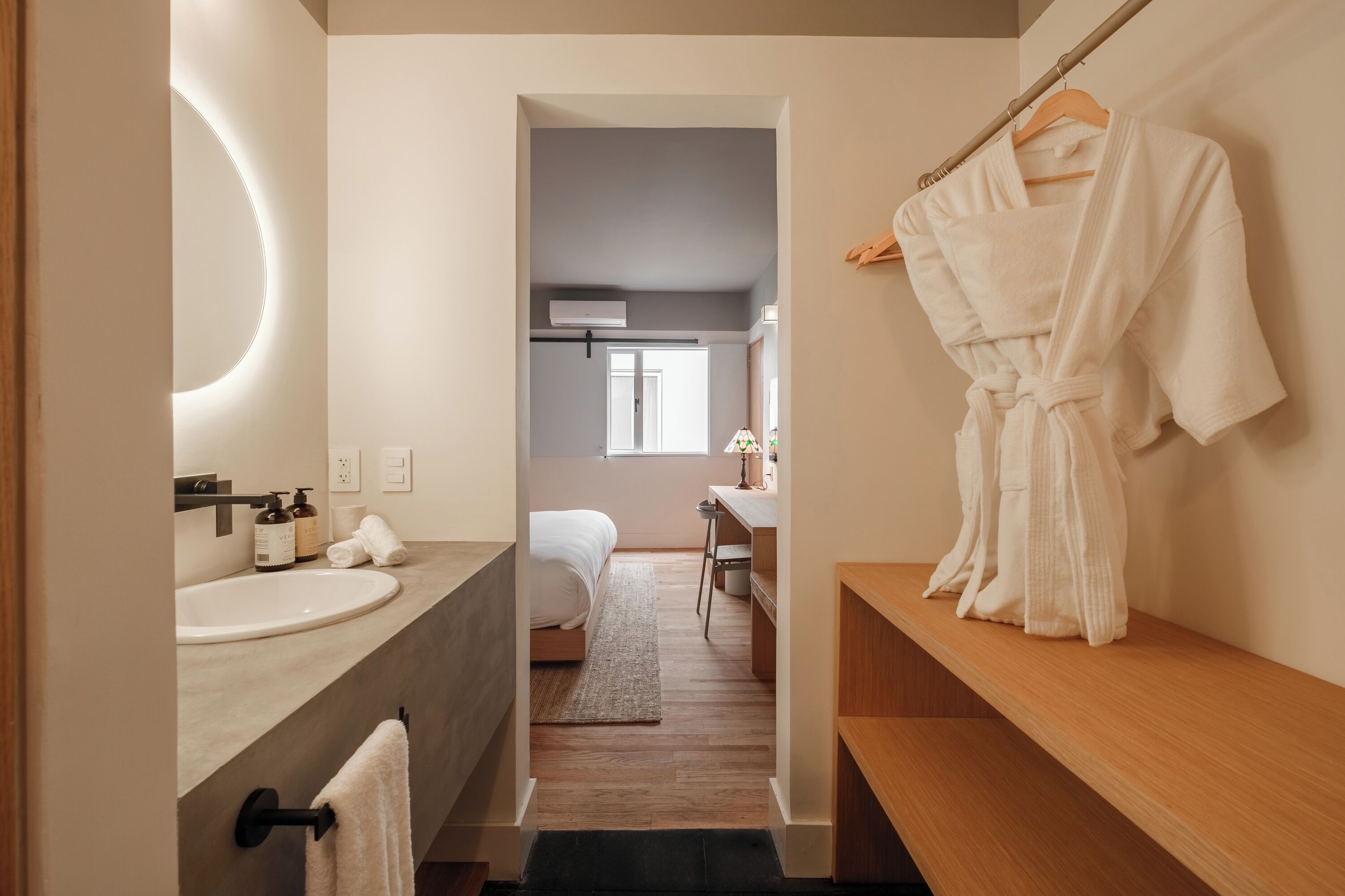 A modern bathroom with a round mirror, a sink, and a robe hanging on a rack.