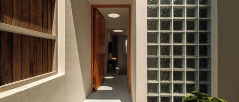 A narrow hallway with a wooden door, a glass block wall, and a ceiling light fixture.