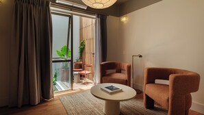 Una sala de estar moderna con una mesa de centro redonda, dos sillones marrones, un ventanal con cortinas y vistas a un balcón con plantas.