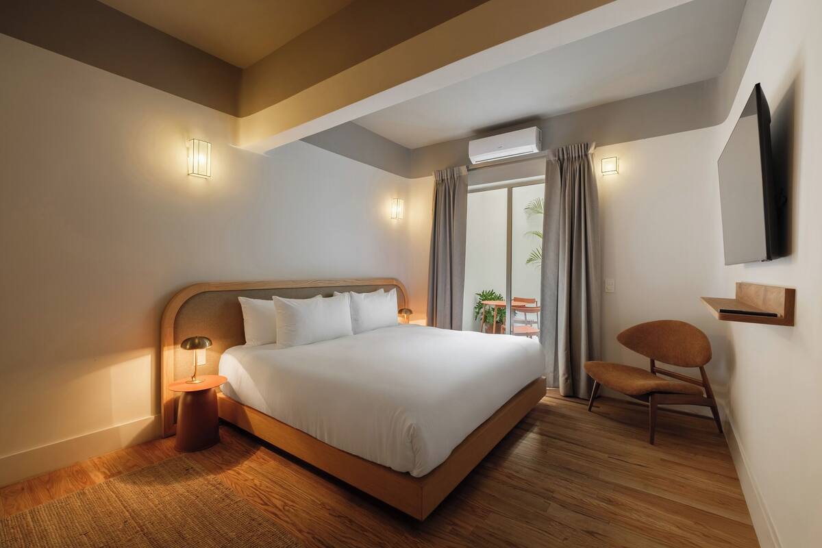 A modern hotel room with a large bed, a bedside table, a chair, and a TV mounted on the wall.