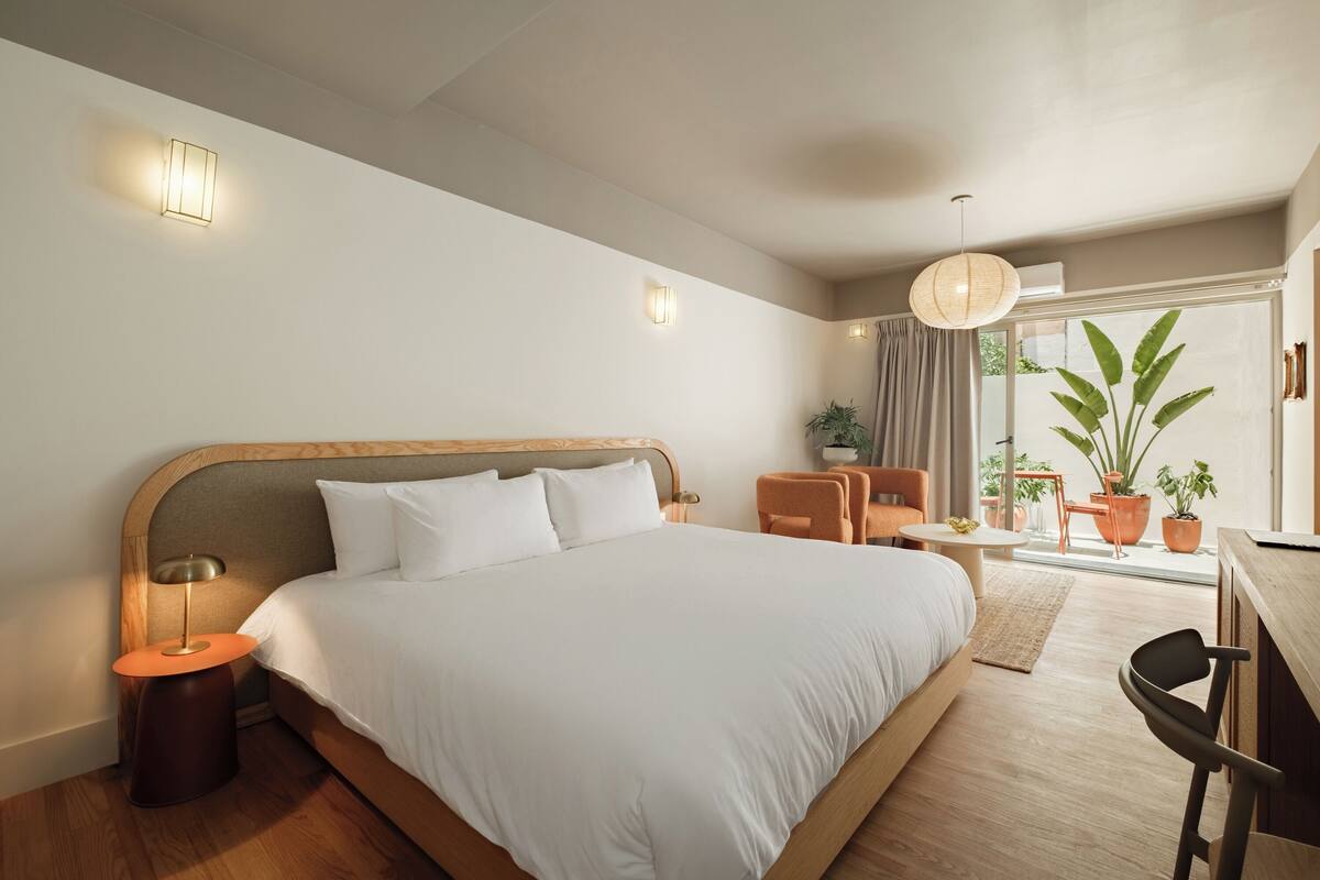 A modern hotel room with a large bed, a desk, and a view of the outdoors.