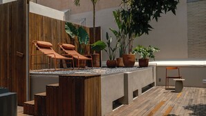 Una terraza en la azotea con sillones de madera, un espacio de descanso de hormigón y plantas en macetas.