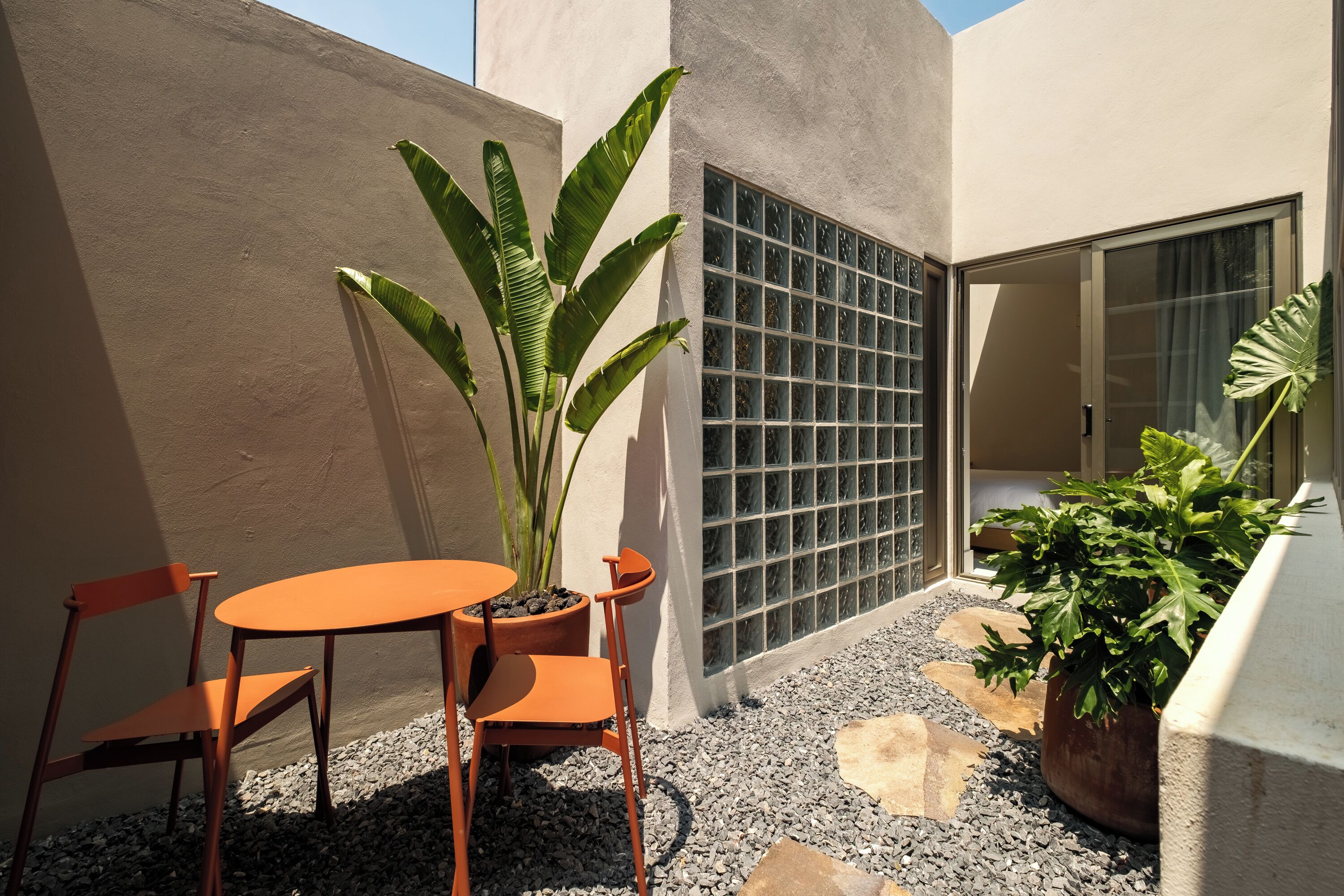 A small outdoor seating area with a table and chairs, surrounded by potted plants and a decorative wall panel.