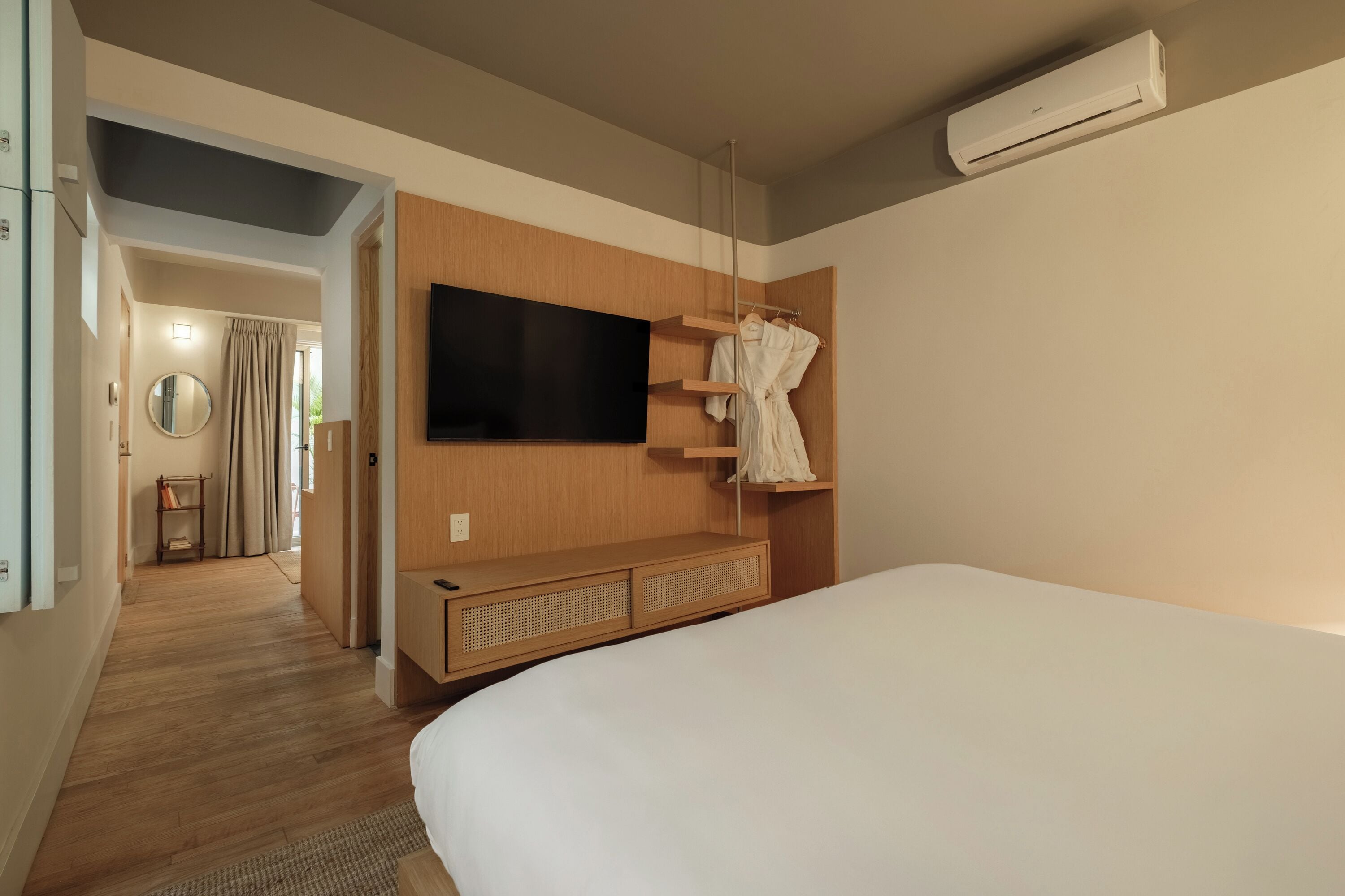 A hotel room with a large bed, a mounted TV, a wooden wardrobe, and a mirror.