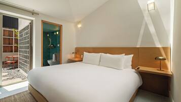 Ein modernes Hotelzimmer mit einem großen Bett, einem Holz-Kopfteil, Nachttischen und einem durch eine offene Tür einsehbarer kleinerem Badezimmer.
