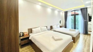 A modern hotel room with two beds, a wooden floor, a small table with a kettle, and a view of the outdoors through a large window. - Mây House Grandworld on the beach (Phu Quoc)