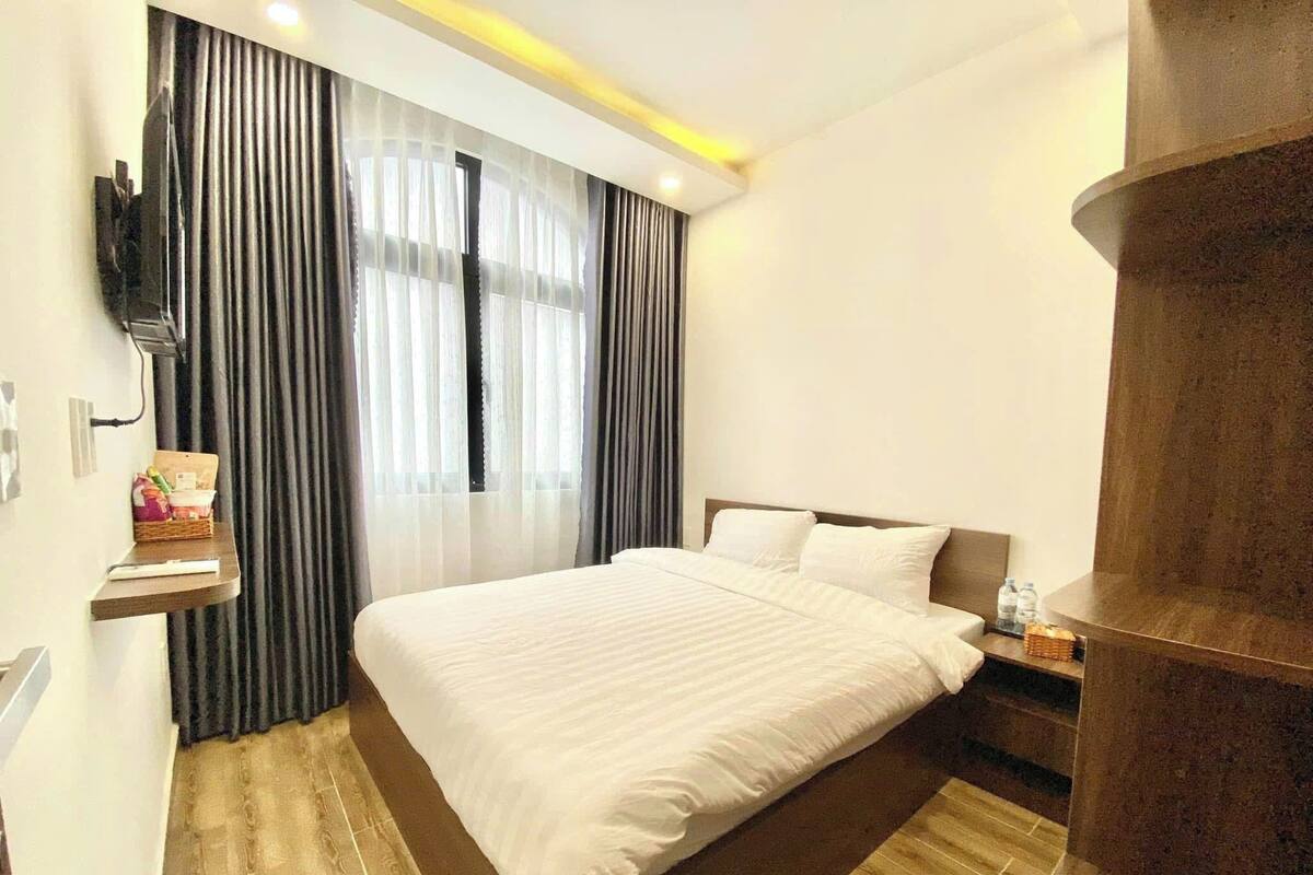 Een hotelkamer met een groot bed, een houten vloer, een aan de muur bevestigde televisie en een raam met gordijnen.