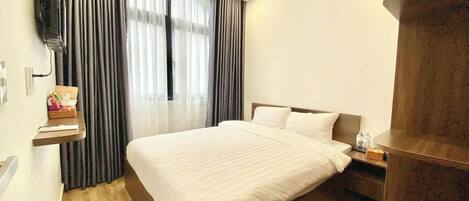 Habitación de hotel con una cama grande, piso de madera, televisor montado en la pared y ventana con cortinas.