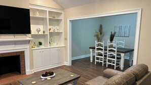 A living room with a fireplace, white built-in shelves, a coffee table, a sofa, and a dining area with a table and chairs.