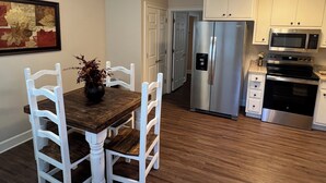 A kitchen with white cabinetry, a stainless steel refrigerator, a microwave, and an oven. There is a dining table with chairs and a vase with flowers.