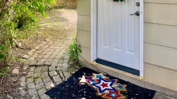 A house with a white door, a flower wreath, and a star-patterned mat.