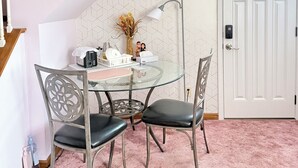 A dining area with a glass table, two chairs, a vase with dried flowers, and a wall-mounted lamp.
