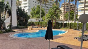 A swimming pool area with lounge chairs and a covered umbrella. - Ground-floor apartment in Frentemar complex for 4 people. (Calp)