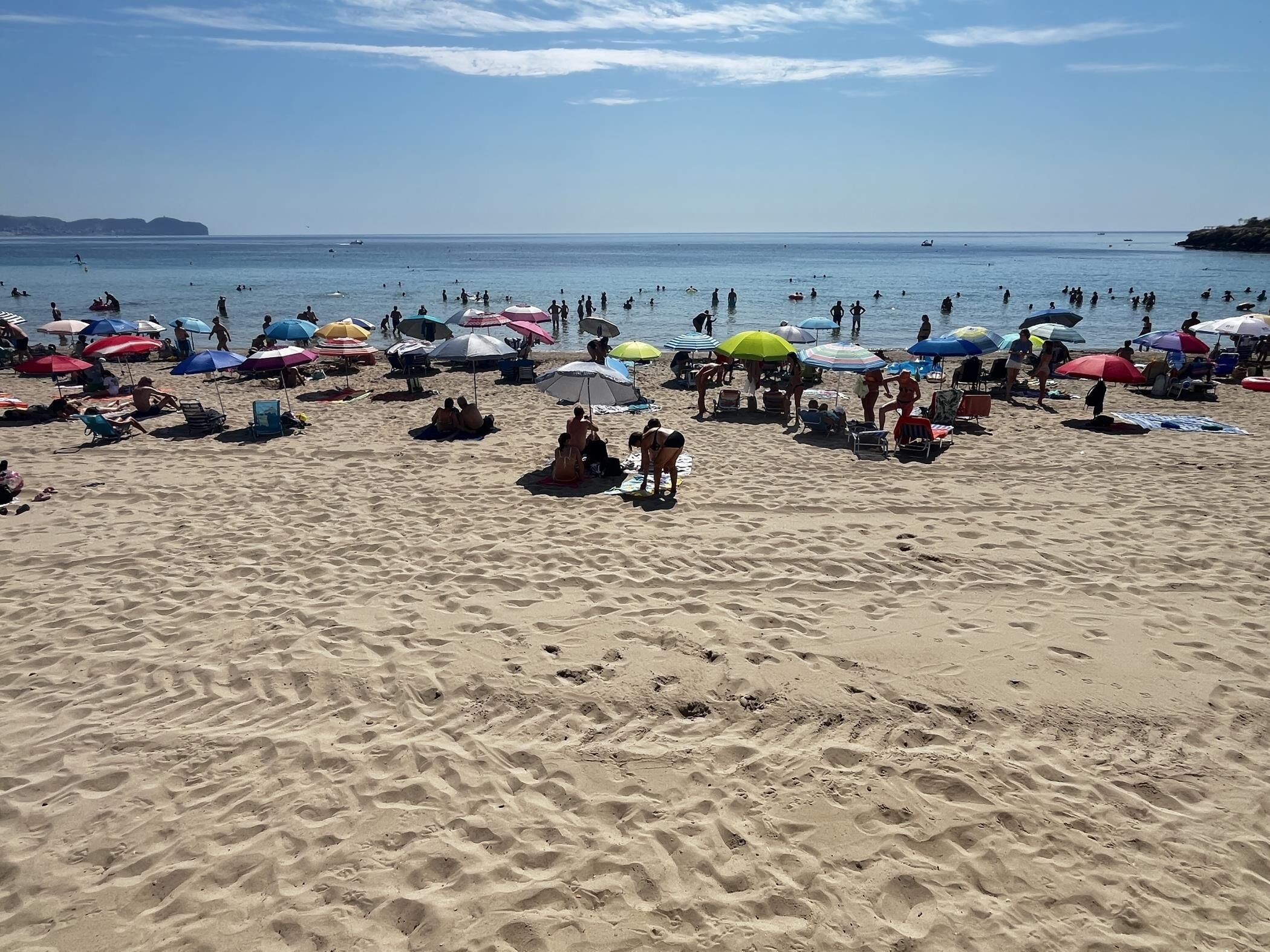Une plage de sable avec de nombreux parasols et des gens qui profitent de l’eau.