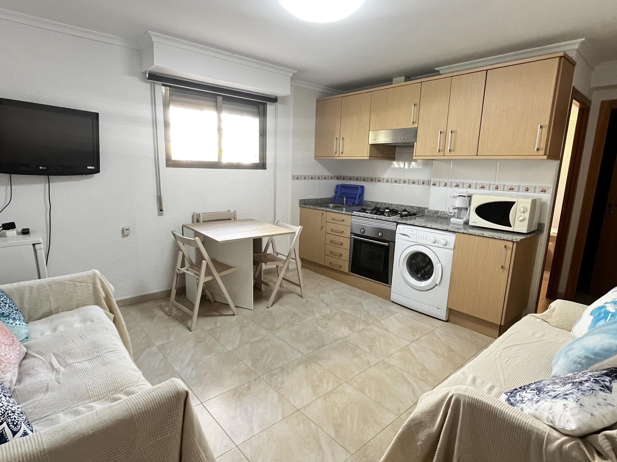 A compact kitchen with a dining table, a washing machine, and a microwave.
