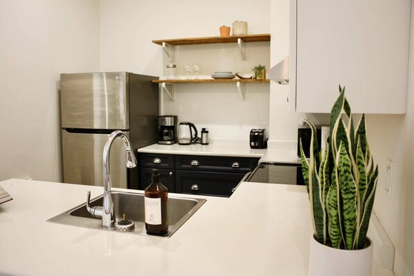 A modern kitchen with a stainless steel refrigerator, a coffee maker, and a sink with a bottle on the counter.