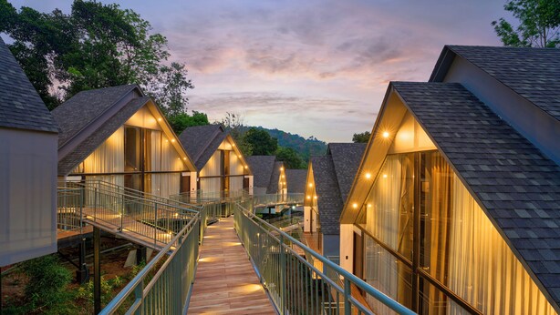 A series of modern cabins with a wooden deck connecting them, surrounded by trees. - Serene Horizon Resort (Kumily)