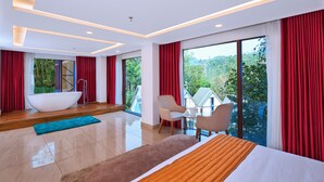 A modern hotel room with a large bed, a bathtub, a seating area, and a balcony with a view of greenery. - Serene Horizon Resort (Kumily)