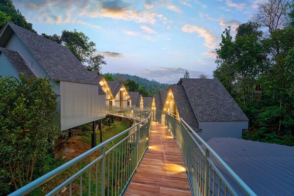 A wooden pathway leading to a row of modern buildings with sloped roofs, surrounded by greenery.