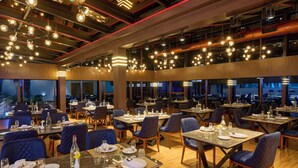 A restaurant with multiple dining tables and chairs, large windows, and hanging light fixtures. - Serene Horizon Resort (Kumily)