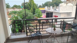 A balcony with a table and chairs, a view of the surrounding buildings, and a signboard. - EASTERN GATE HOMESTAY (Rajnagar)
