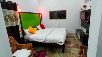 Quarto com uma cama, uma cadeira, uma mesinha e uma prateleira com objetos.