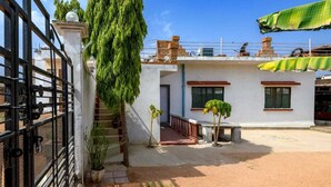 A residential building with a white exterior, a small staircase leading to a balcony, and a metal gate. - EASTERN GATE HOMESTAY (Rajnagar)