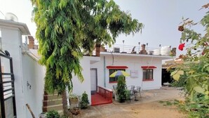A building with a red and white facade, a gated entrance, and a small outdoor seating area with a table and chairs. - EASTERN GATE HOMESTAY (Rajnagar)