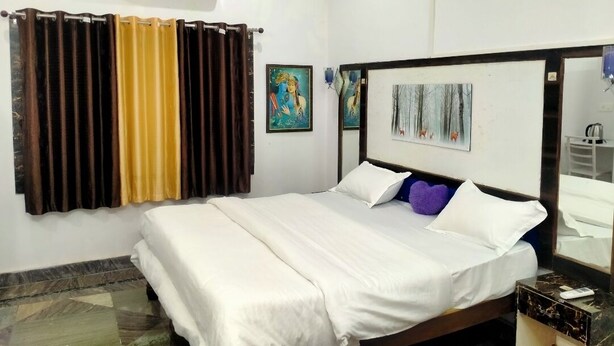 A hotel room with a bed, a bathroom mirror, a wall-mounted air conditioner, and two paintings. - EASTERN GATE HOMESTAY (Rajnagar)
