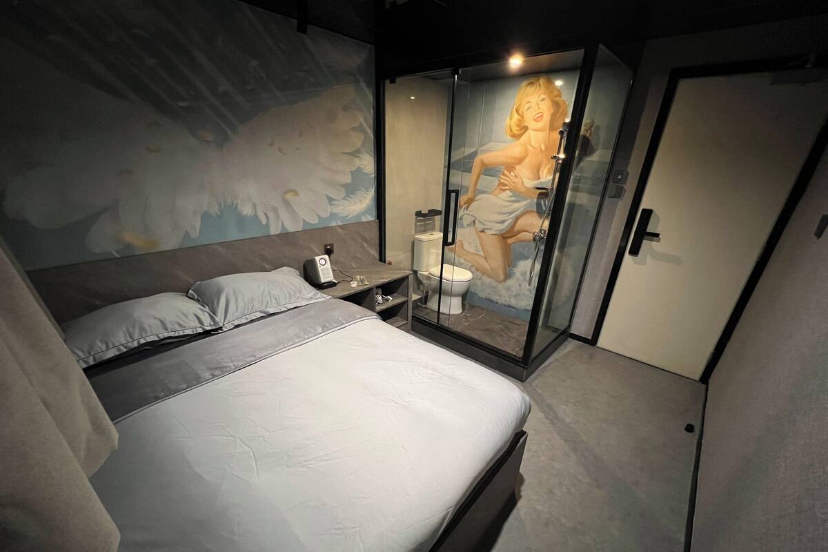 A modern bedroom with a bed, a nightstand, a glass-enclosed shower, and a mural on the wall.