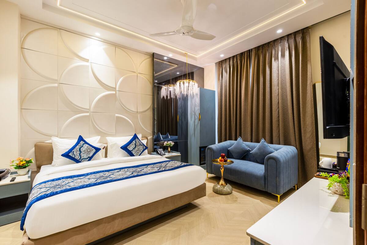A modern hotel room with a large bed, a sofa, a flat-screen TV, and a ceiling fan.