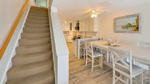 Eine moderne Küche mit weißen Schränken, ein Essbereich mit weißem Tisch und Stühlen sowie eine Treppe mit hölzernem Geländer.