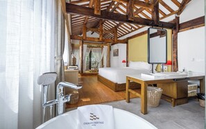 A hotel room with a wooden ceiling, a large bed, a bathroom with a bathtub, and a table with a mirror.