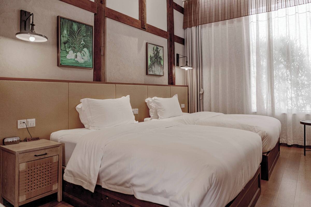 A hotel room with two beds, a nightstand, and a small table.