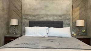 A bedroom with a large bed, two bedside tables, and a herringbone-patterned wall.