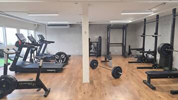Ein Fitnessraum mit Laufbändern, einer Hantelbank und Gewichte.