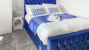 A neatly made bed with a blue upholstered headboard, white linens, and a decorative tray with a cup and saucer. - 2 bedroom accommodation in Inverness (Inverness)