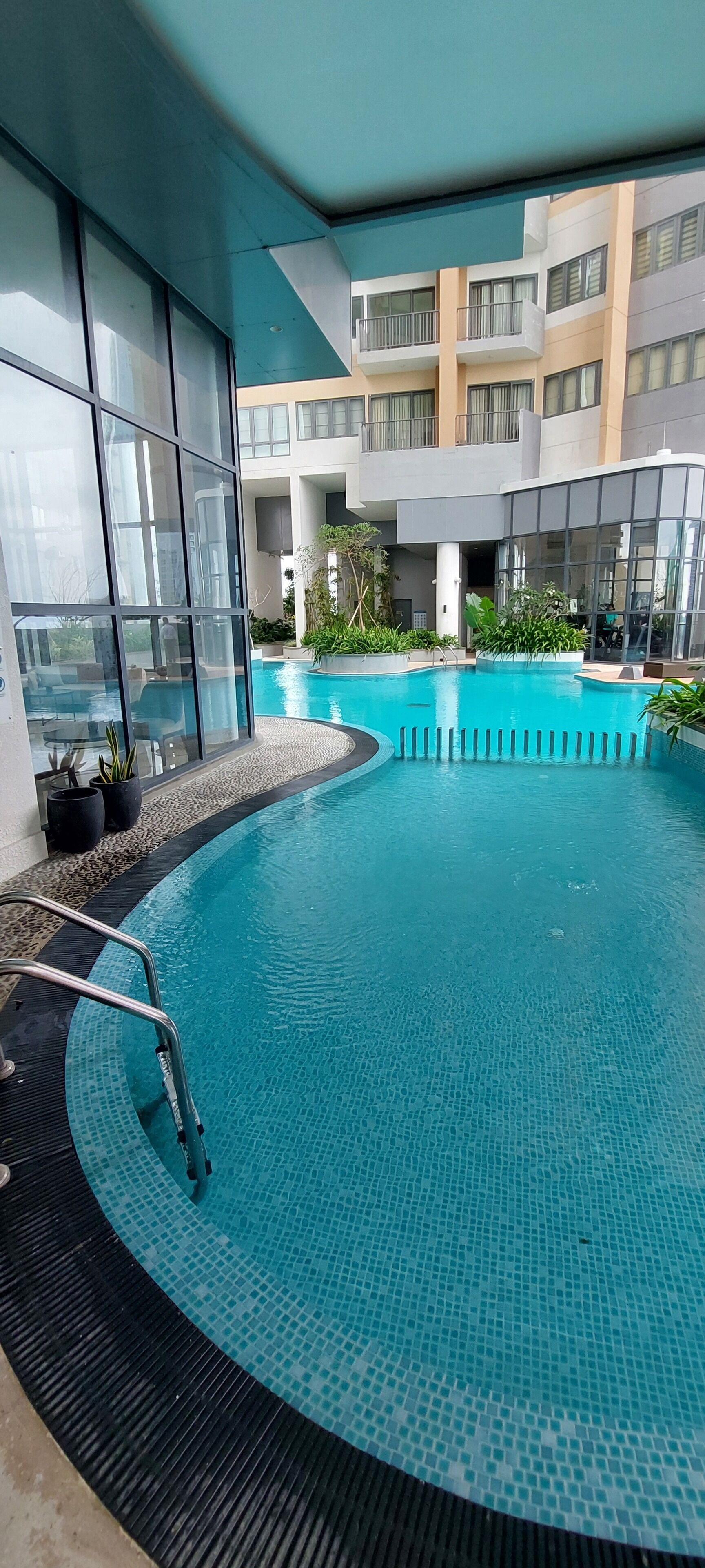 A modern indoor swimming pool with clear blue water, surrounded by glass walls and potted plants.