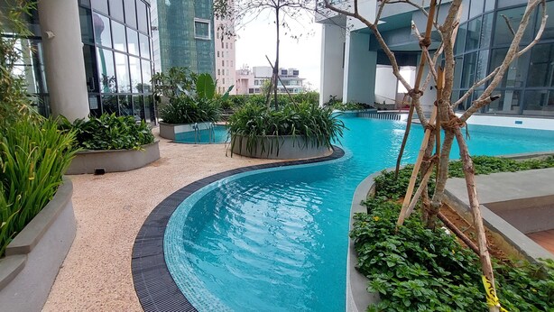 A modern indoor pool area with a curved design, surrounded by planters with various plants, and large windows reflecting the surrounding buildings. - Nine Peaks Summit TriZen  (Colombo)