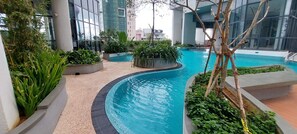A modern indoor pool area with a curved design, surrounded by planters with various plants, and large windows reflecting the surrounding buildings. - Nine Peaks Summit TriZen  (Colombo)