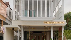 Un hotel de dos pisos con un balcón, un letrero que dice "TEN BOUTIQUE HOTEL", y un área de entrada cubierta con plantas.