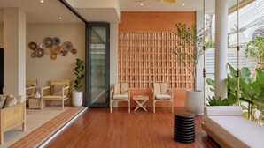 Una sala de estar moderna con piso de madera, una puerta de vidrio que da a otra habitación, y un espacio de descanso con dos sillones y un sofá.