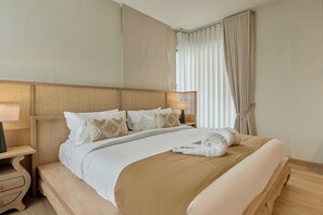 Una cama bien hecha con una colcha color beige y almohadas blancas, un cabecero de madera y una mesita de noche con una lámpara.